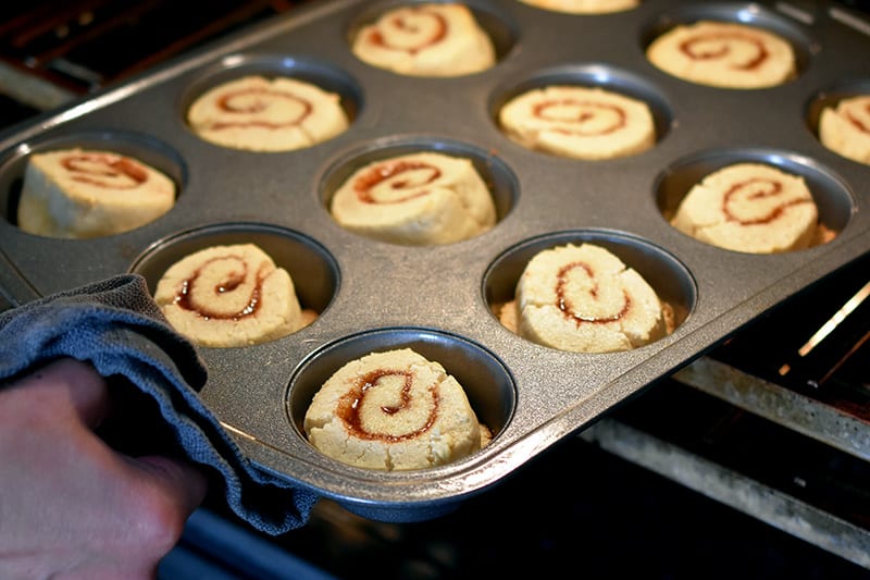 Rotating the muffin pan filled with paleo cinnamon rolls halfway through the baking process.