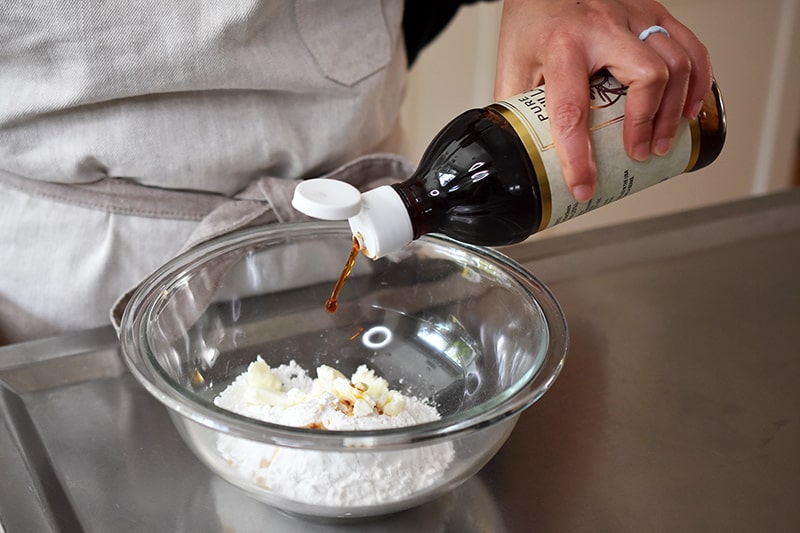 Pouring vanilla extract into a bowl filled with the paleo cinnamon roll frosting ingredients.
