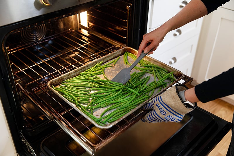 Tossing the roasted green beans with a gray silicone spatula midway through roasting.