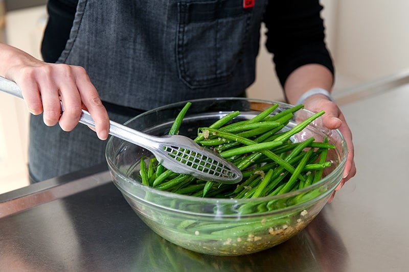 Someone tossing green beans in a Whole30 and keto-friendly lemon and garlic marinade.