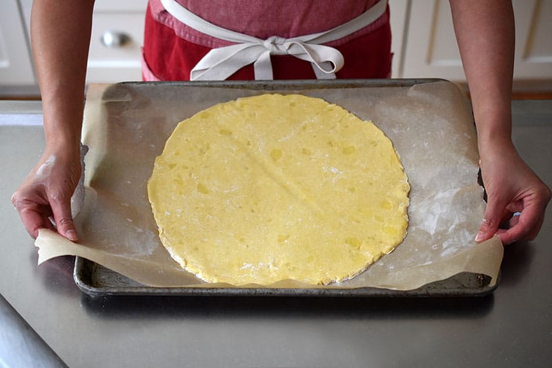 Someone placing the rolled out paleo galette dough on a parchment lined rimmed baking sheet.