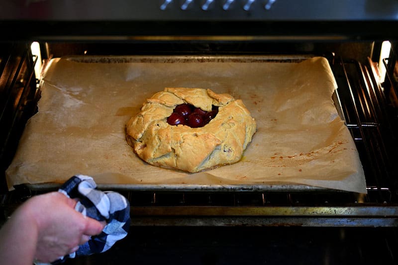 Rotating the cherry galette at the halfway baking point to ensure even browning.