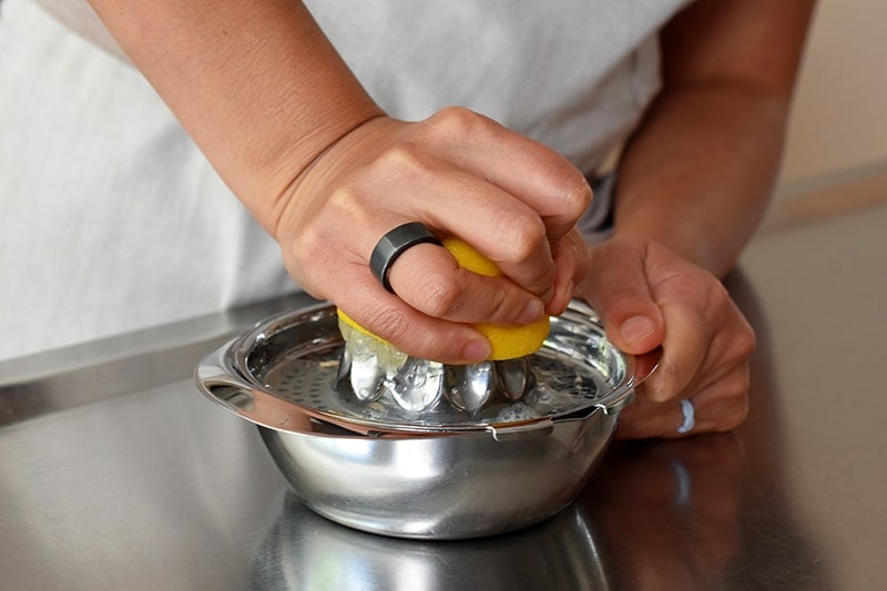 Someone juicing a lemon with a stainless steel citrus juicer.