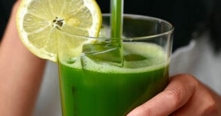A woman in a white apron is taking a sip from a glass of matcha lemonade.