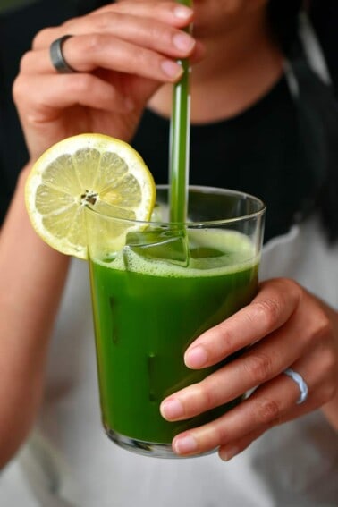 A woman in a white apron is taking a sip from a glass of matcha lemonade.