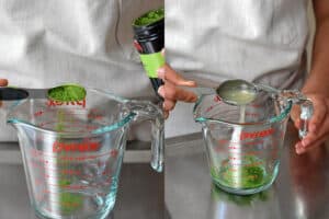 Adding a spoonful of matcha and lemon juice into a liquid measuring cup.