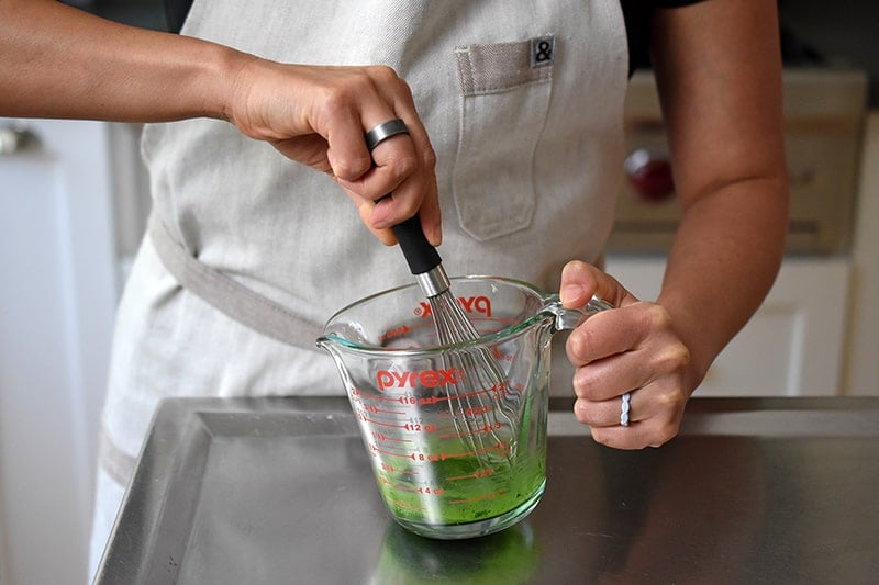 Someone whisking together matcha and lemon juice in a measuring cup.