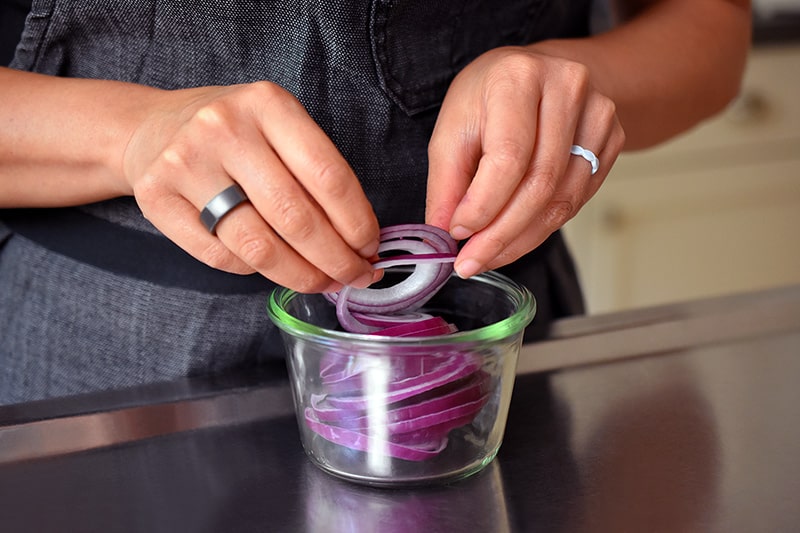 Someone adding thin red onion slices in an open Weck jar.