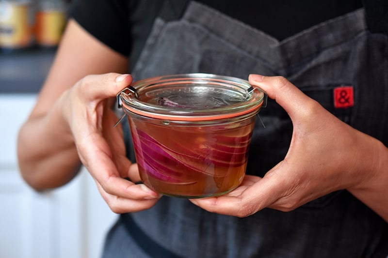 Two hands holding a clear glass jar filled with quick pickled red onions.