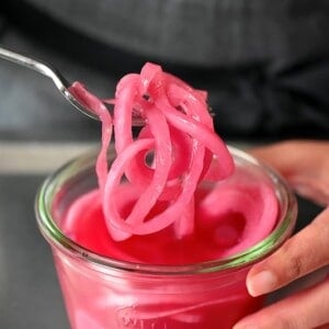 A fork pulling up a bunch of quick pickled red onions from a jar.