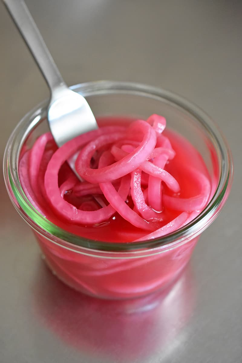 A fork removing quick pickled red onions from an open clear glass jar.