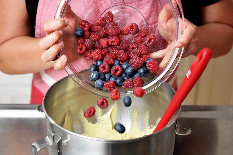 Adding blueberries and raspberries to a mixing bowl to make paleo berry snack cake.
