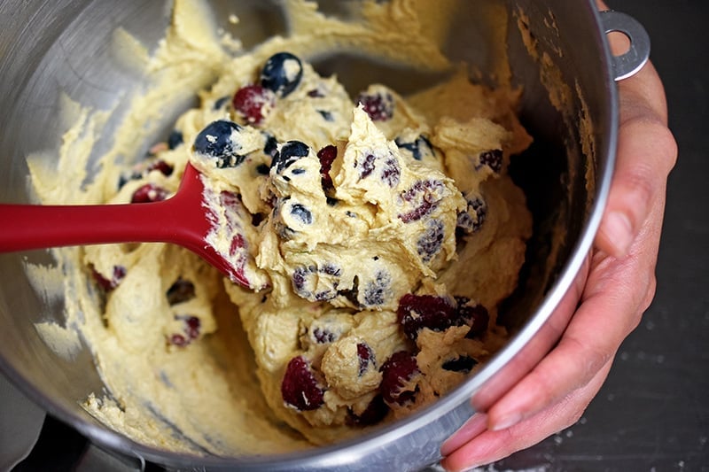 A red silicone spatula is folding in the berries in the berry snack cake batter.