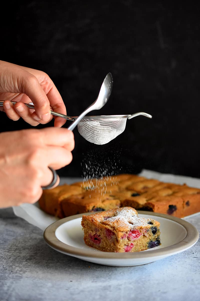 Someone adding sifted keto confectioners sugar onto the paleo berry snack cakes