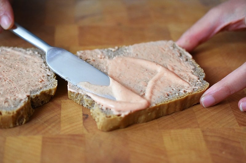 A knife is spreading sriracha mayonnaise on a slice of gluten-free and paleo sandwich bread.