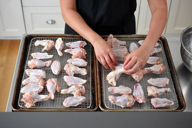 Arranging chicken wings in a single layer on wire racks in two rimmed baking sheets .