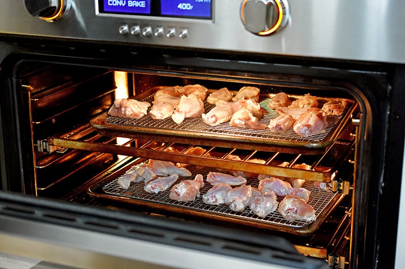An open oven with chicken wings on two different racks.