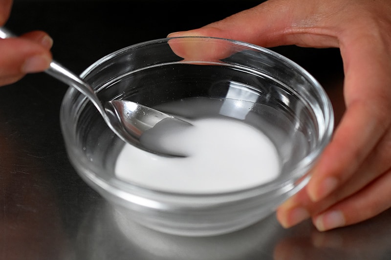 A small glass bowl filled with arrowroot and water and stirred with a spoon.