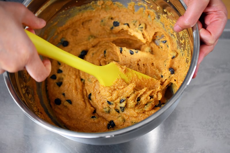 Folding in the chocolate chips into the pumpkin muffin batter with a yellow silicone spatula.