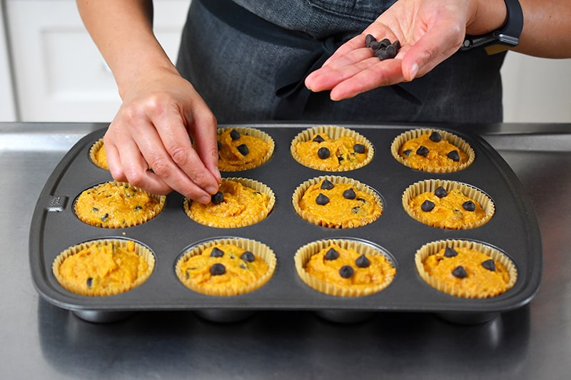 Adding extra chocolate chips on top of the pumpkin chocolate chip muffins before placing them in the oven.