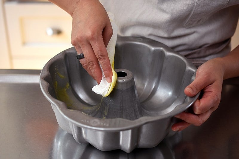 Someone using a paper towel to grease a 10-inch bundt pan with ghee.