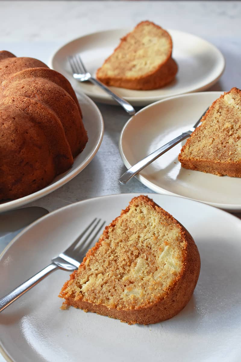 A shot of three slices of apple Bundt Cake on white plates with forks, next to the cake.