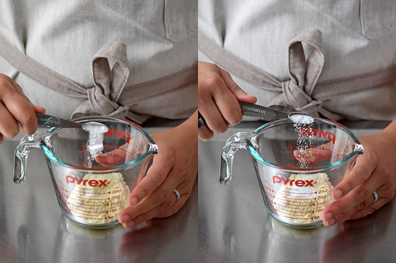 A hand is adding salt and baking soda to a liquid measuring cup filled with almond flour.