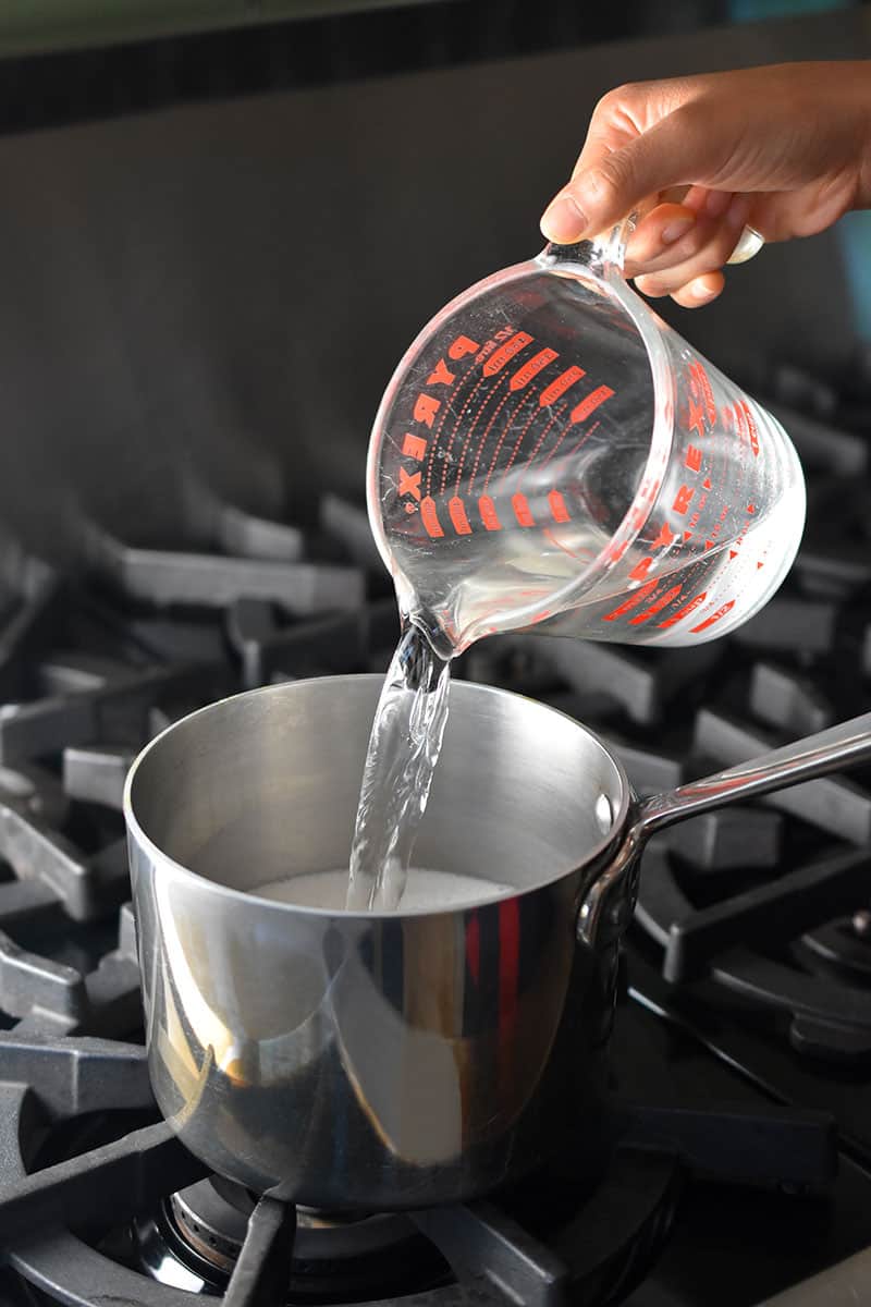 Pouring water from a Pyrex measuring cup into a saucepan on the stovetop to make Golden Milk.