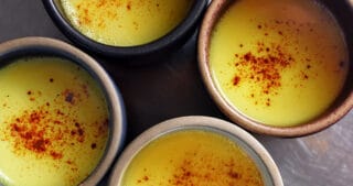 An overhead shot of four mugs filled with Golden Milk topped with ground cinnamon