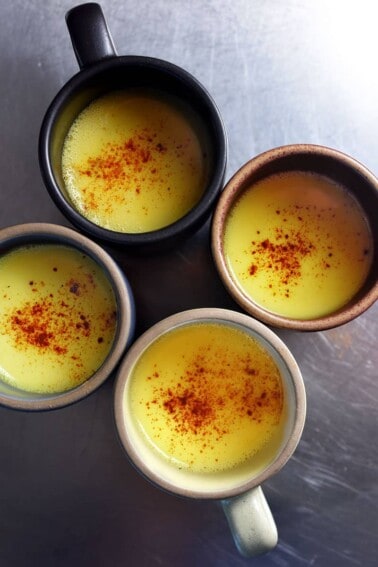 An overhead shot of four mugs filled with Golden Milk topped with ground cinnamon