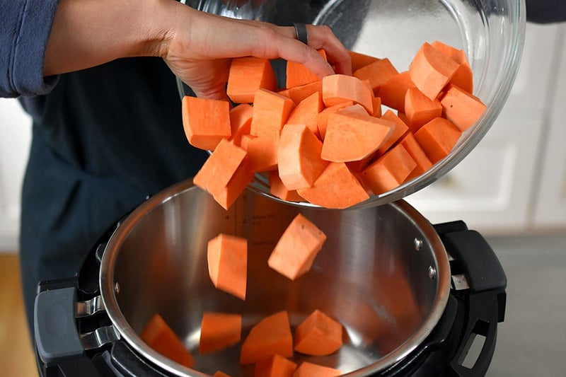 Someone dumping sweet potato cubes into an open Instant Pot