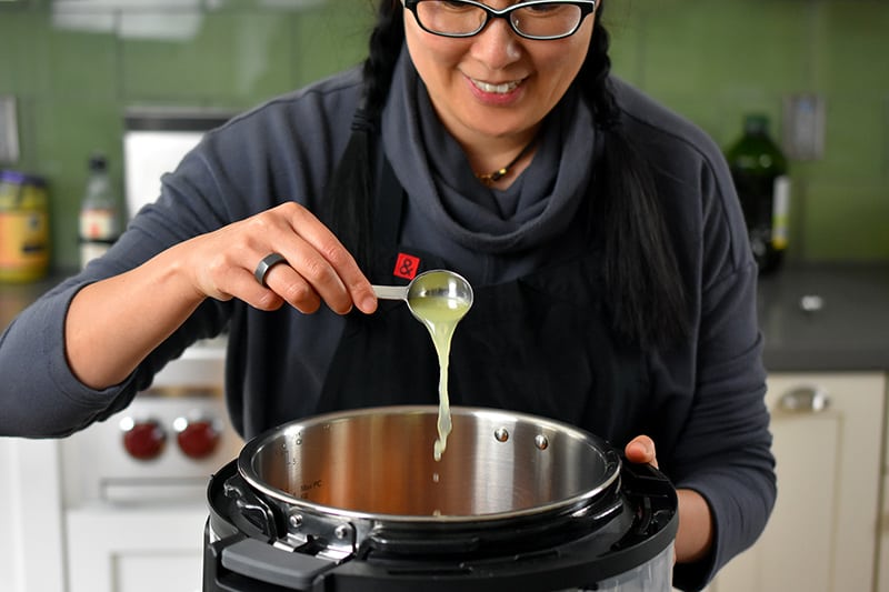 A brunette smiling lady is pouring fresh lime juice into an open Instant pot