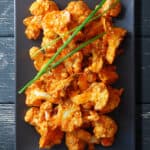 An overhead shot of baked buffalo cauliflower on a rectangular gray plate. There are three chives on top.