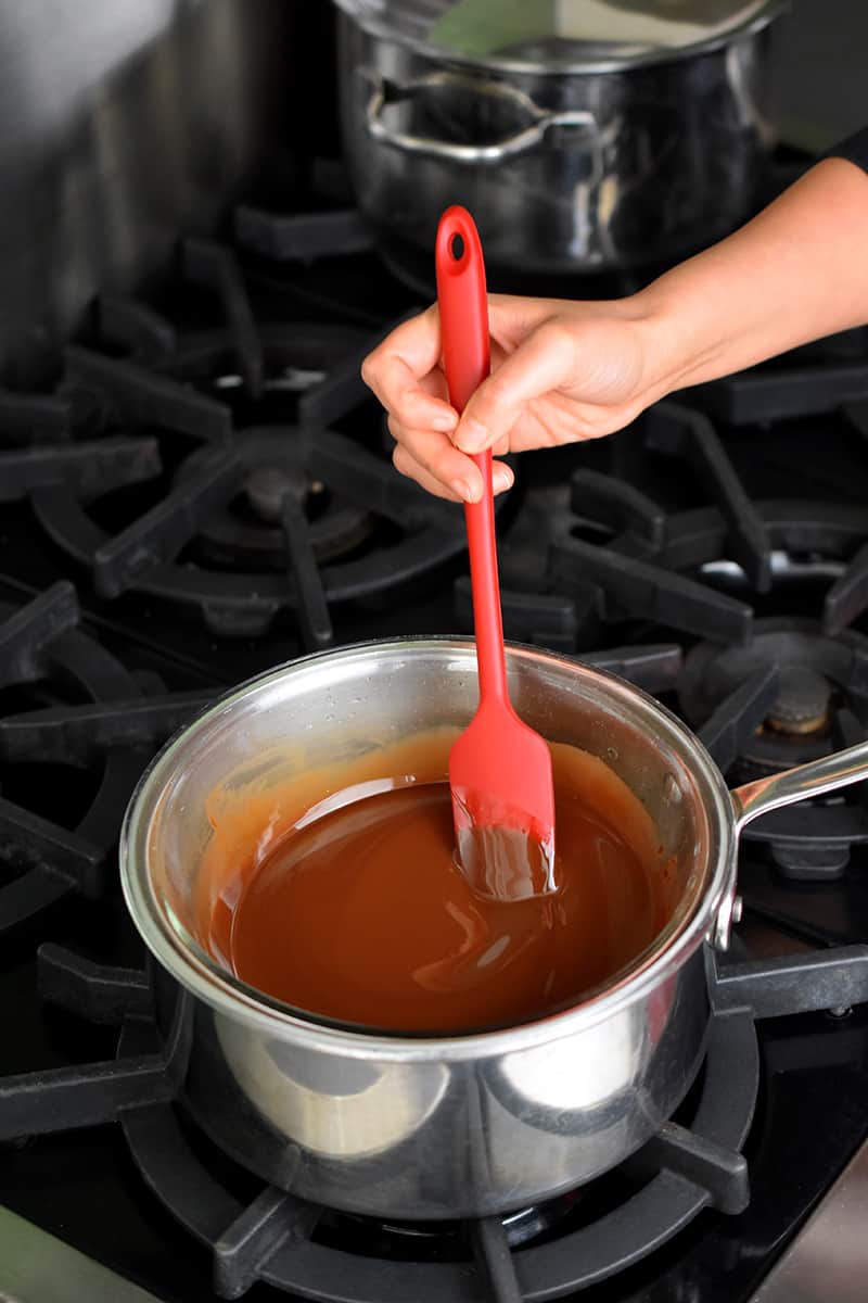 A bowl is filled with melted chocolate on top of a saucepan. A red silicone spatula is in the bowl.