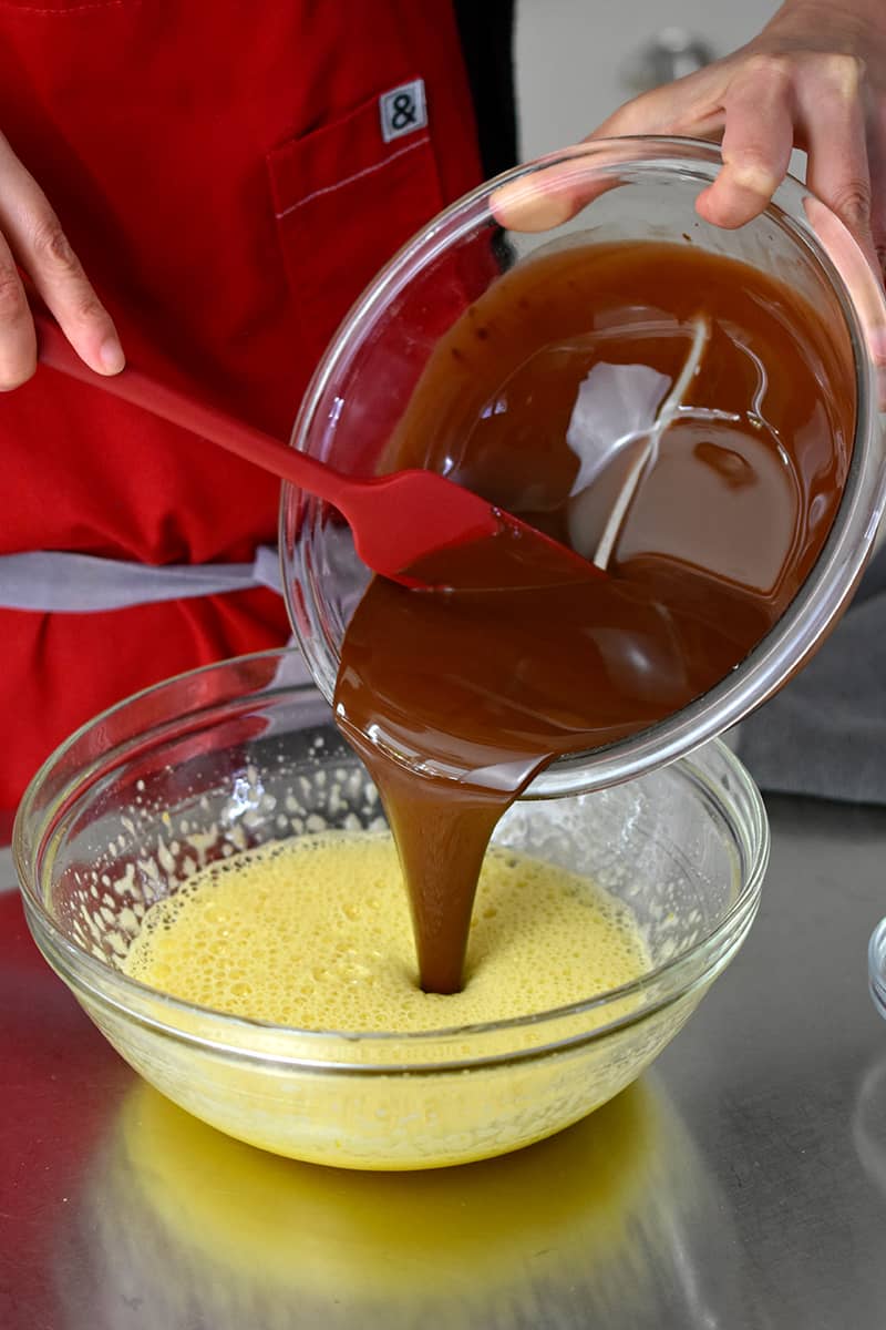 Pouring a bowl of melted chocolate and ghee into the egg mixture. 