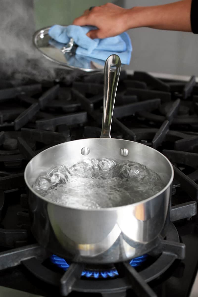 A stainless steel saucepan is filled with boiling water on a stovetop.