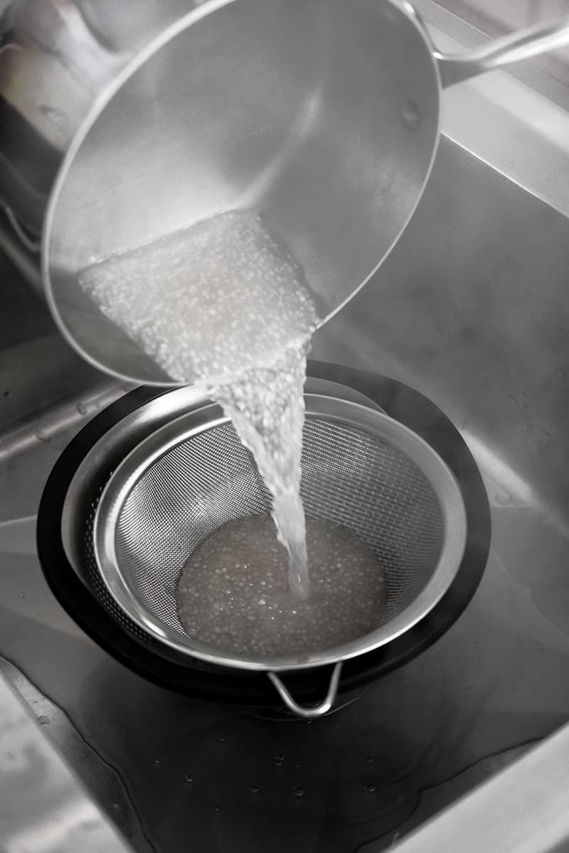 A closeup of a saucepan pouring cooked small tapioca pearls into a fine mesh sieve in a colander.