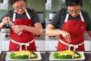 An Asian woman in a red apron is adding fresh cracked pepper and chopped chives on top of a platter of Asparagus Mimosa