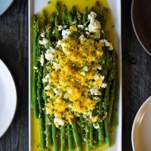 An overhead shot of a rectangular plate filled with Asparagus Mimosa, cooked asparagus tossed with a lemon vinaigrette and topped with chopped hard boiled eggs and chives.