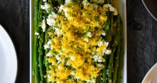 An overhead shot of a rectangular plate filled with Asparagus Mimosa, cooked asparagus tossed with a lemon vinaigrette and topped with chopped hard boiled eggs and chives.