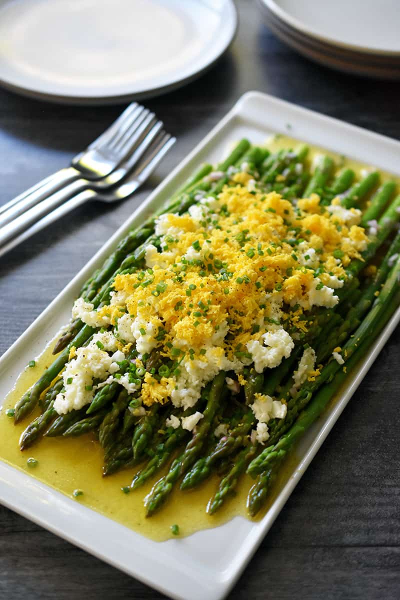Side shot of Asparagus mimosa on a rectangular white platter with forks and plates on the side.