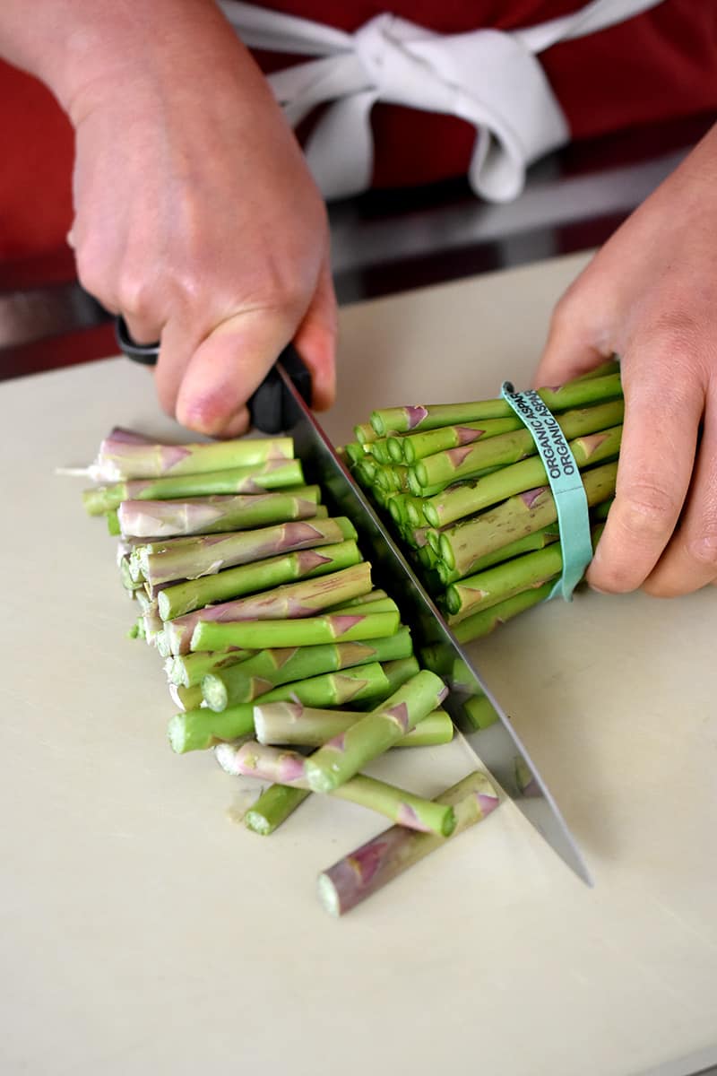 An overhead shot of someone trimming the woody ends off of a bunch of asparagus.