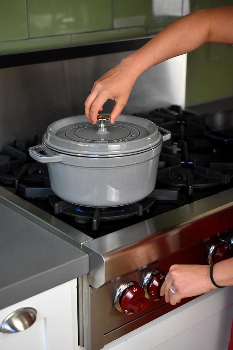A hand putting the lid on a gray stockpot filled with water on the stove.