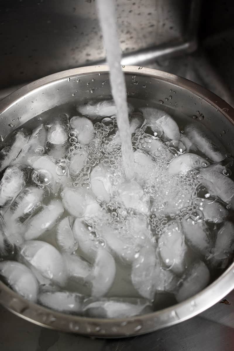 A large silver bowl with ice is being filled with water.