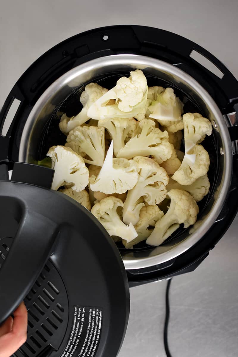 An overhead shot of an open Instant Pot filed with cauliflower florets in a streamer.