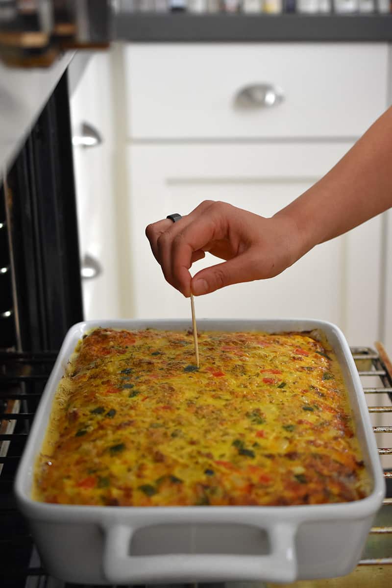 A hand is poking a toothpick in a finished Mexican Breakfast Casserole.