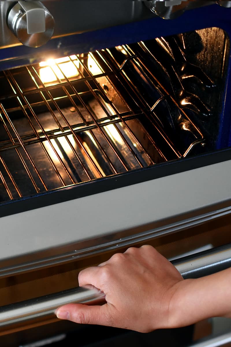 A hand is opening an oven and you can see that the rack is in the middle of the oven.