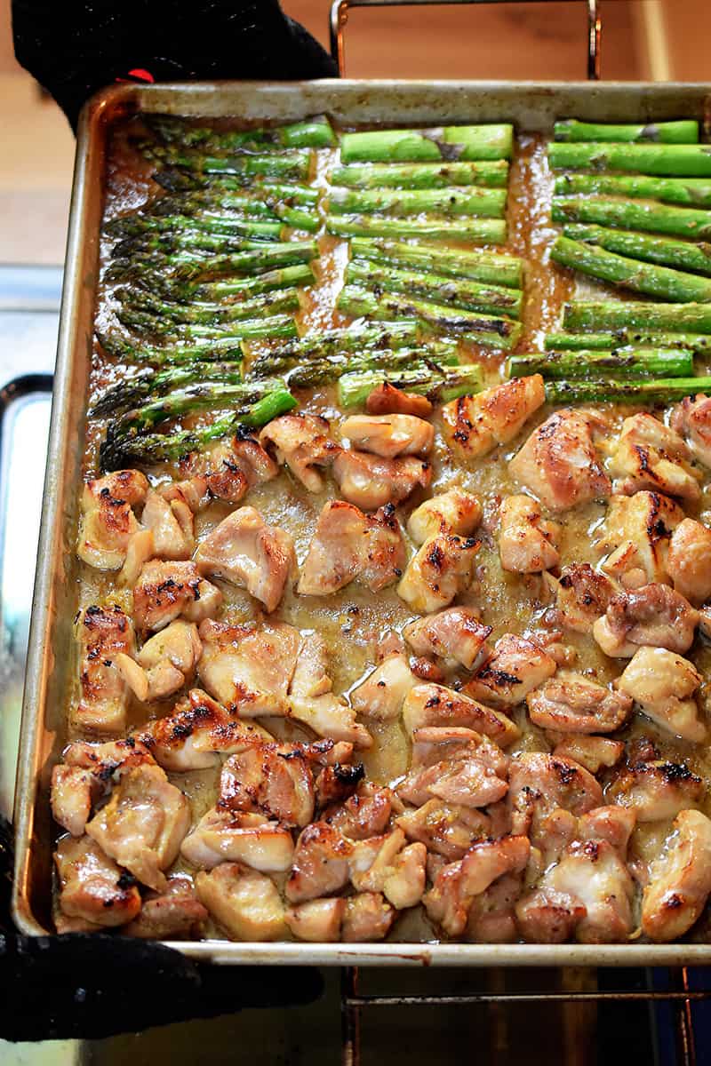 An overhead shot of sheet pan chicken and asparagus ready to be removed from the oven. The chicken and asparagus are browned all over and the sauce is slightly thickened.