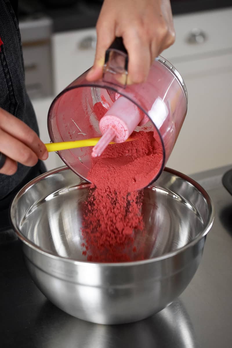 Someone pouring powdered freeze dried strawberries from a small food processor to a large silver bowl.