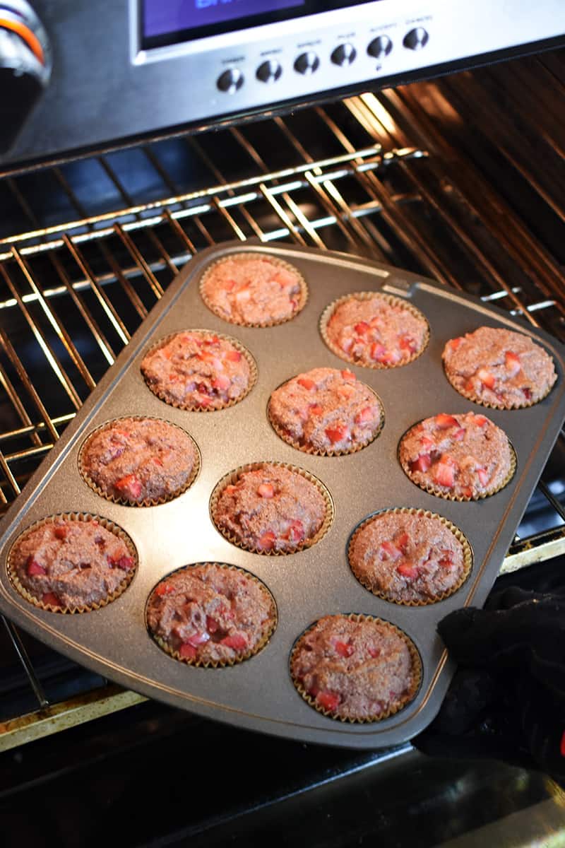 Someone is rotating a muffin pan filled with strawberry muffins at the halfway point of baking.